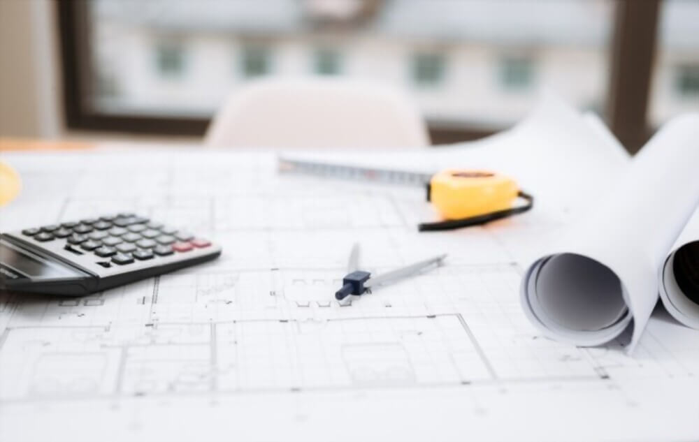 Architectural plans, calculator and measuring tools used in construction cost estimating.
