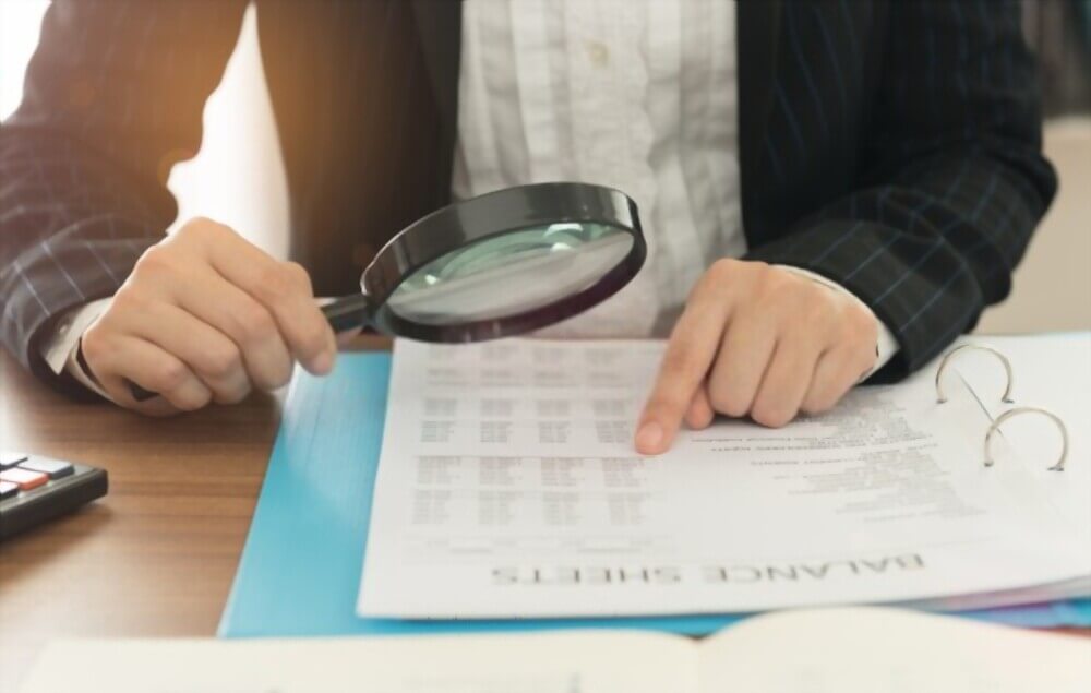 Financial document review using magnifying glass during construction audit process